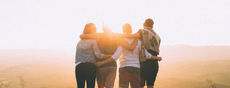 A view of the back of four friends hugging and looking into the sunset