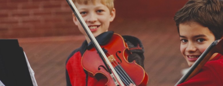 Two smiling boys with a cello and violin ready to perform